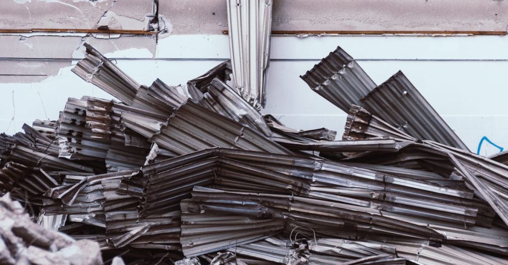 Pile of corrugated metal sheets against a worn industrial wall.