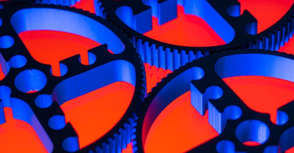 Colorful macro image of blue metallic gears against a red background, highlighting engineering precision.