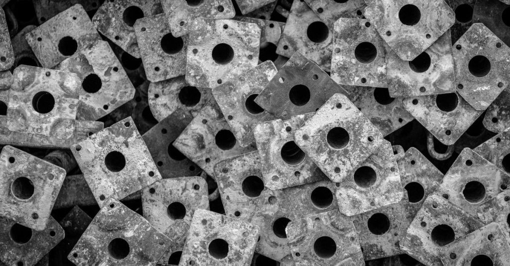A close-up abstract composition of stacked, perforated metal plates in black and white, showcasing texture and pattern.