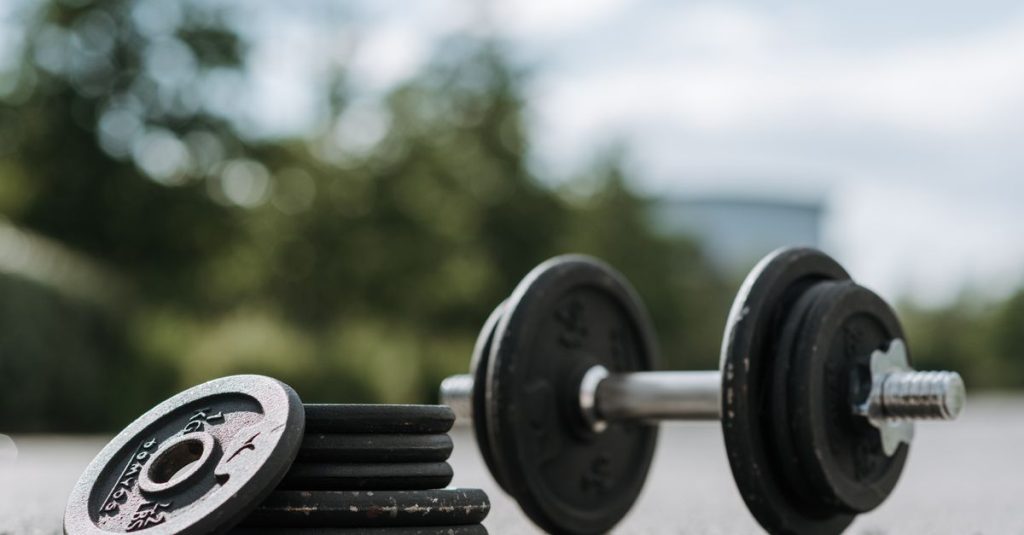 Ground level of dumbbell with metal bar and pile of cast iron plates on roadway under cloudy sky