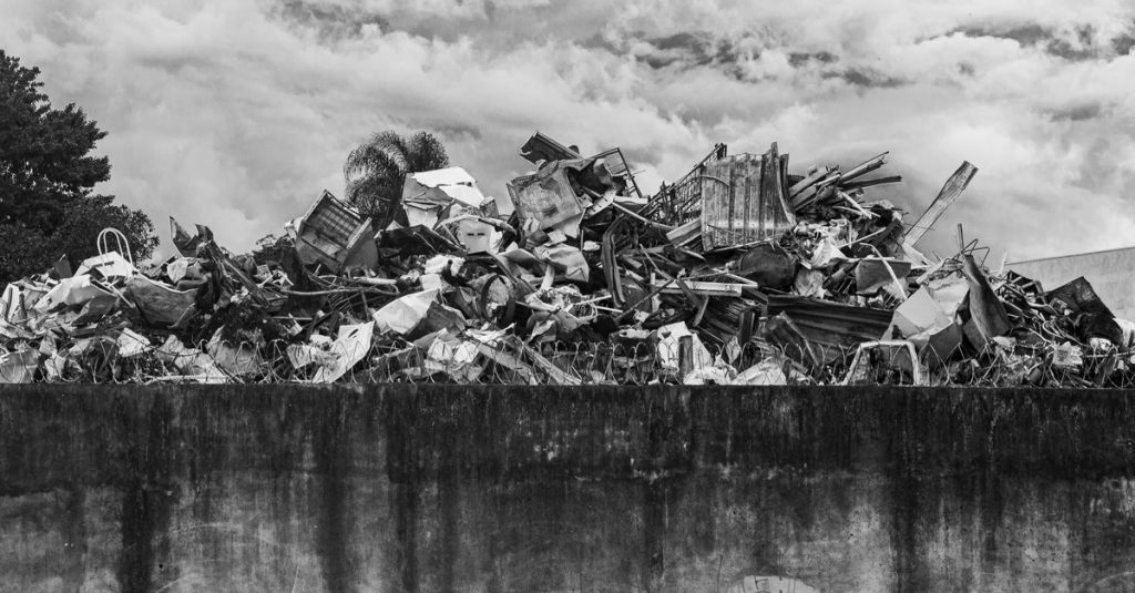 A layered pile of scrap metal against a cloudy sky, captured in black and white for a dramatic effect.