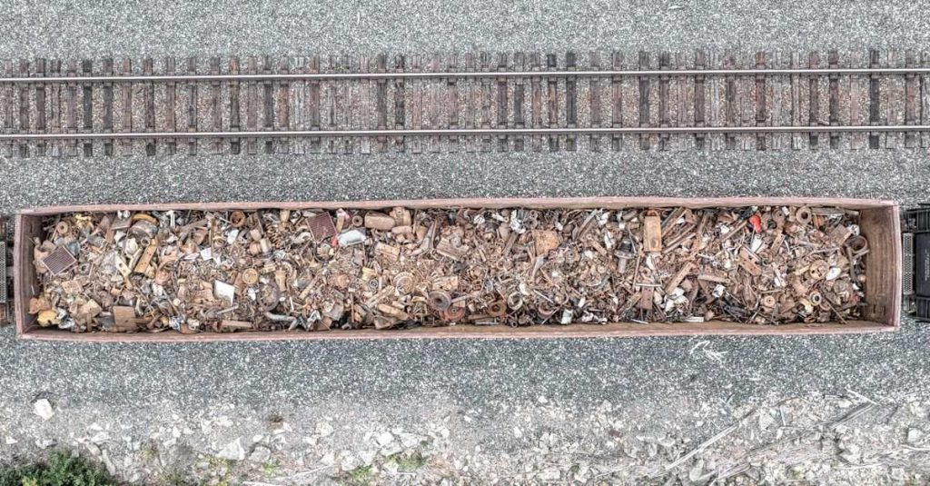 An aerial shot of a cargo train carrying rusty scrap metal along railway tracks.