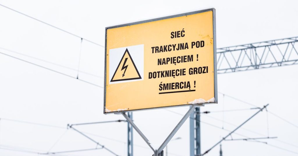 Yellow warning sign in Polish with electric symbol, cautioning about high voltage on railway lines.