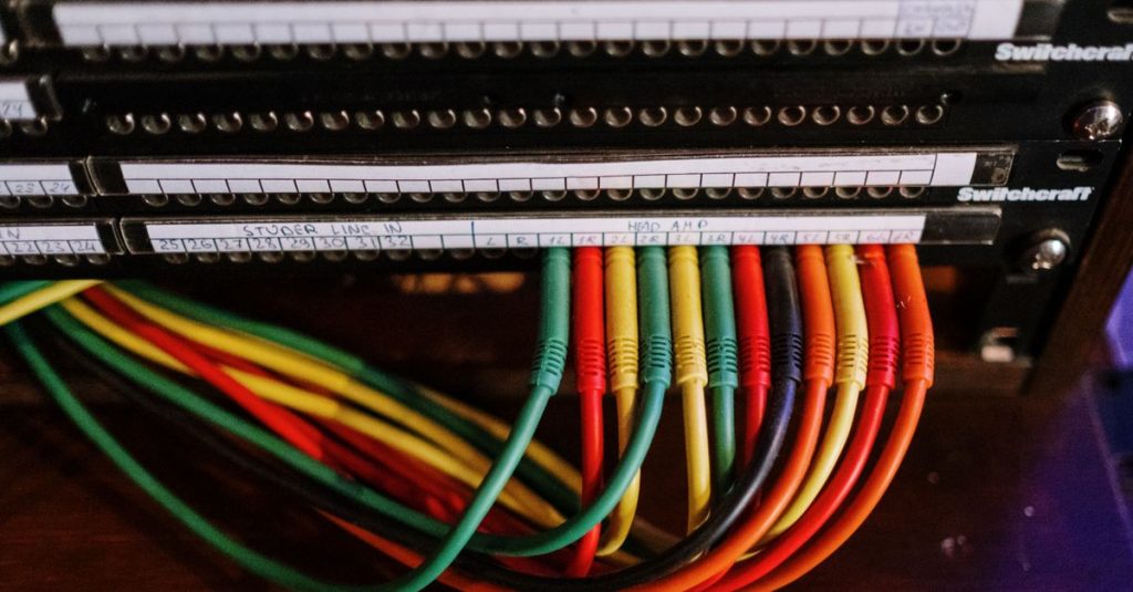 Close-up of colorful patch cables connected to a network panel with labels, indoors.