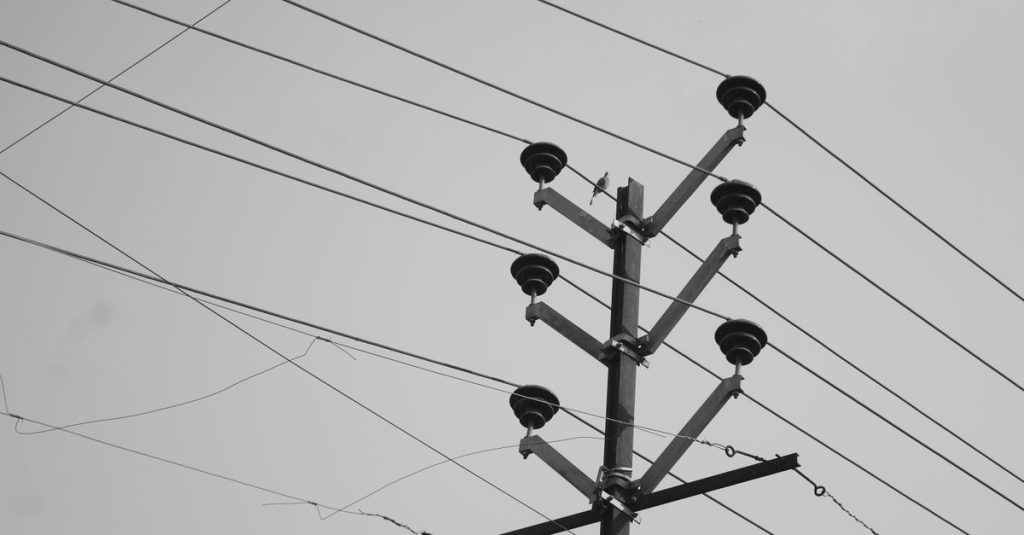 A low angle monochrome photo of a utility pole with power lines against the sky.