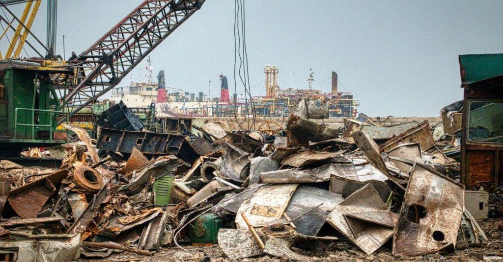Metal crane located near heap of rusty litter against ships in port city