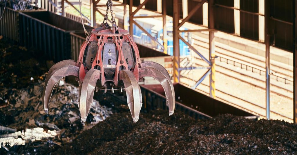 A claw crane inside a recycling facility lifting scrap metal, highlighting industrial processes.