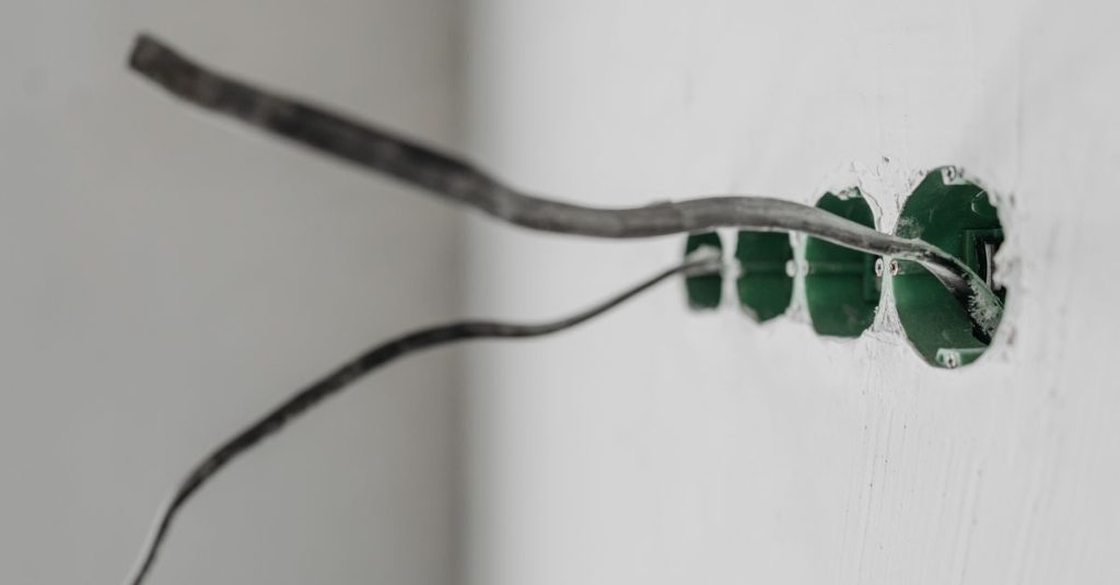 Unfinished electrical outlet installation with exposed wires on a white wall.