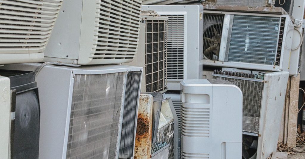 A collection of various old and broken air conditioning units piled outdoors.