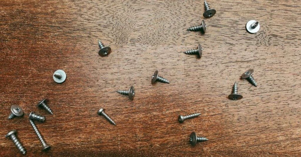 Overhead view of various screws scattered on a wooden surface, ideal for construction themes.
