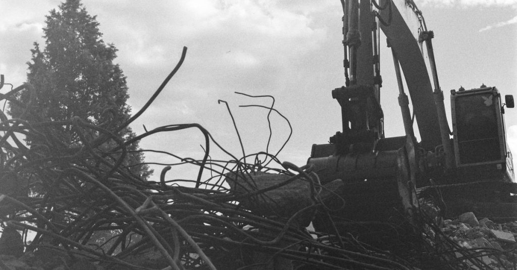 Monochrome image of an excavator engaged in demolition amidst rubble and debris.