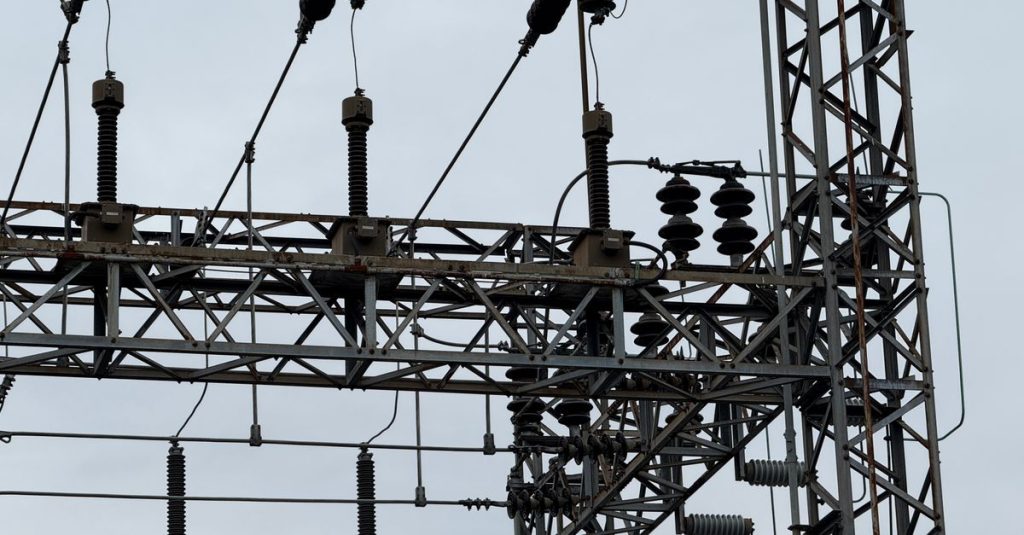 Close-up of high voltage power lines with intricate metal structures against a cloudy sky.