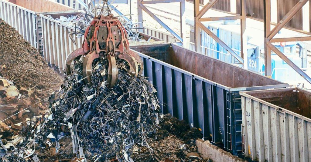 An industrial claw crane lifts metal scrap in a recycling facility, showcasing efficient waste management.