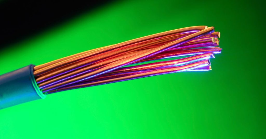 Close-up of colorful copper electrical wires against a vibrant green backdrop, showcasing vivid contrasts and textures.