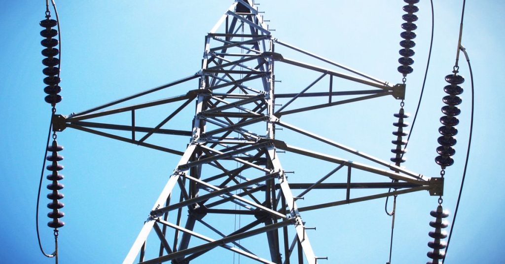 Low angle view of an industrial power transmission tower against a clear blue sky.