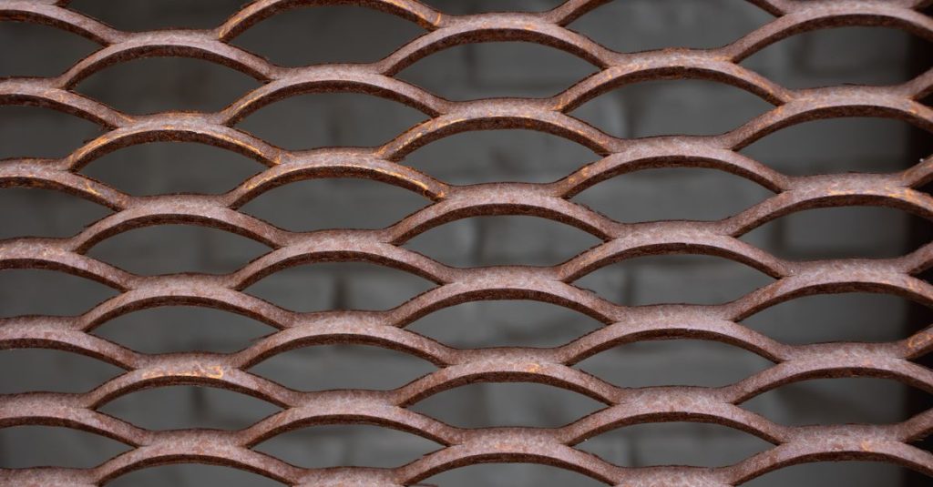 Closeup of textured backdrop of metal oval wall with symmetrical holes against blurred gray brick wall