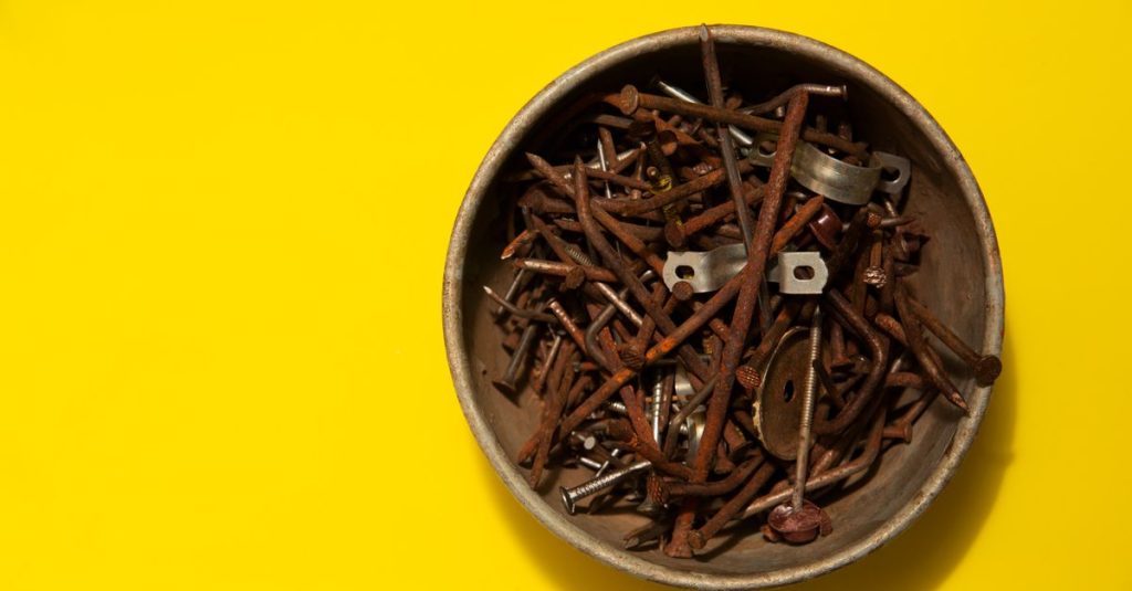 A bowl filled with assorted rusty nails on a vivid yellow background, top view.
