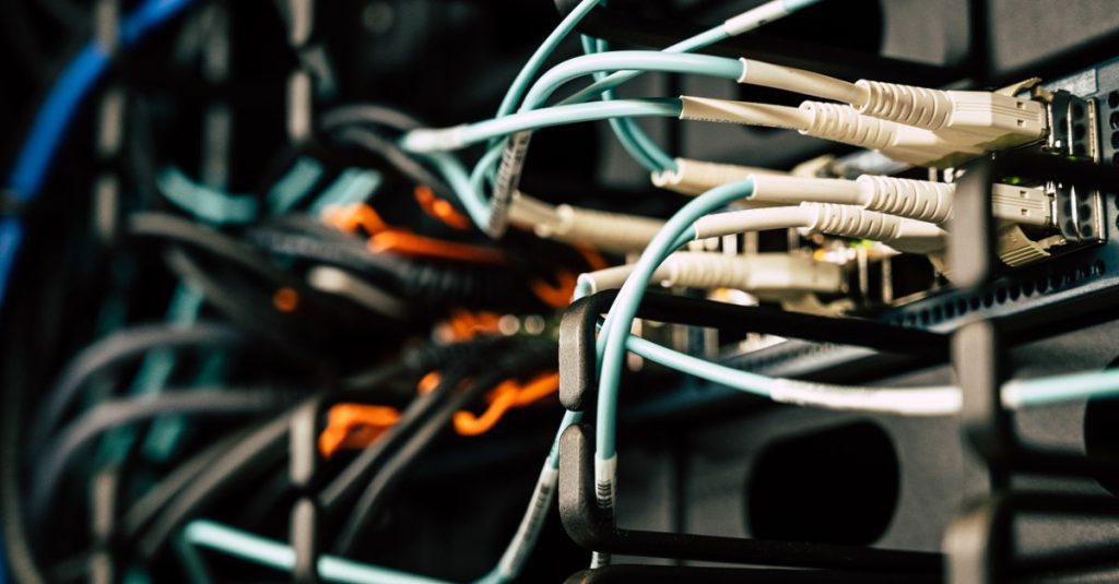 Various tangled wires connected to system near black metal cases in server room