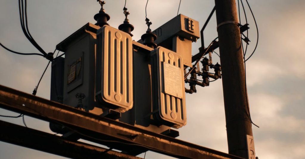 Close-up of an electrical transformer on a utility pole against a sunset sky.