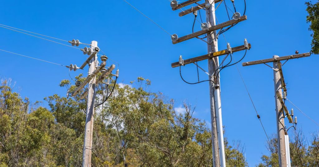 Wooden utility poles with power lines and a blue sky backdrop. Ideal for energy and utility themes.