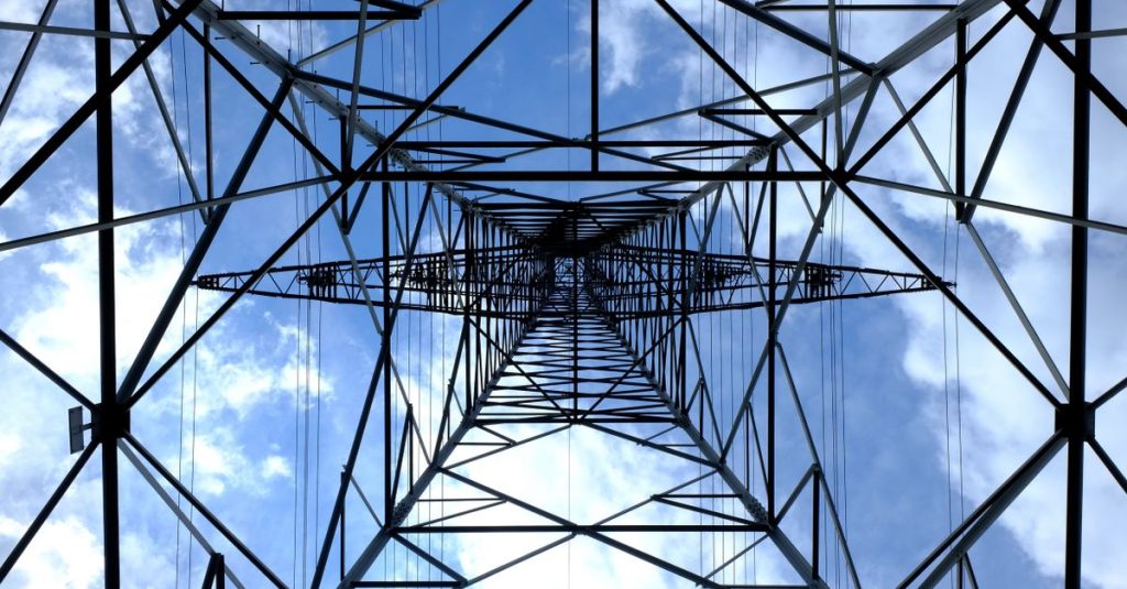 Looking up at a steel power pylon against a bright blue sky.
