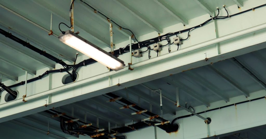 Detailed view of industrial ceiling light and wiring at a low angle in an indoor setting.