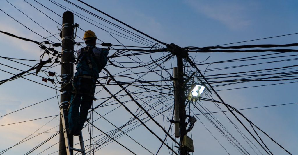 Silhouette of an electrician fixing power lines at sunset in Ubud, Bali.
