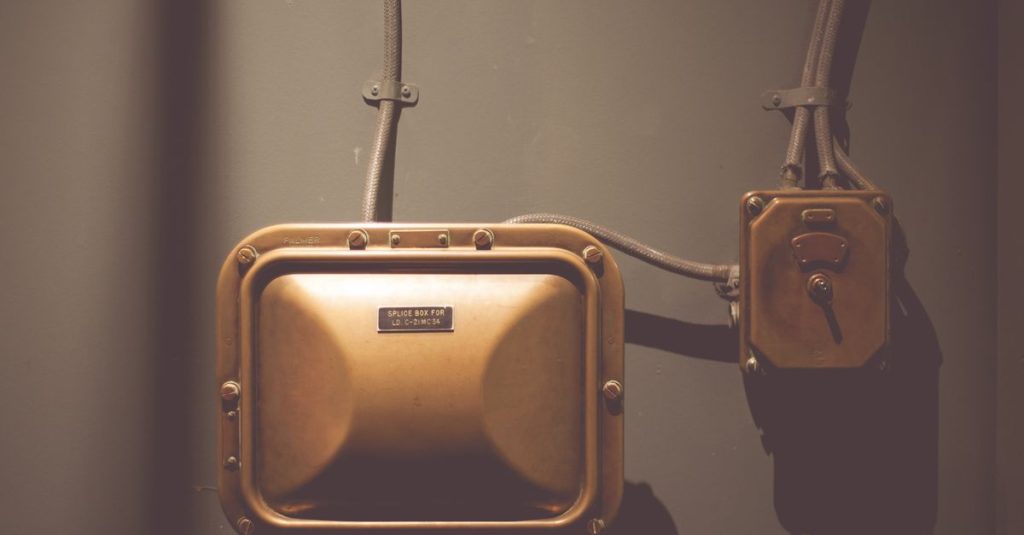 Industrial electrical control box with vintage design and copper finish on a wall.