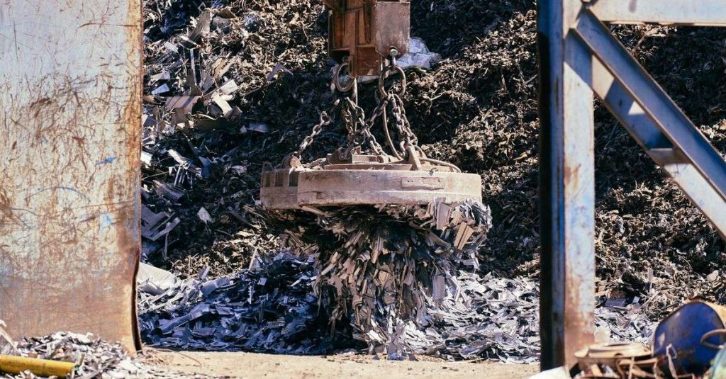 Magnet crane lifting scrap metal in a recycling yard.