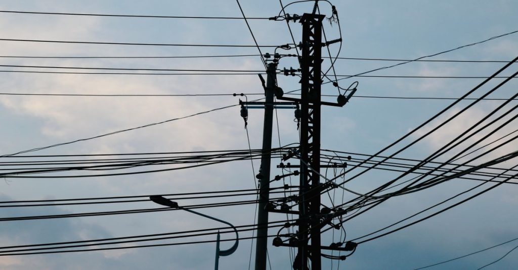 A complex network of power lines and pylons silhouetted against a bright sky.
