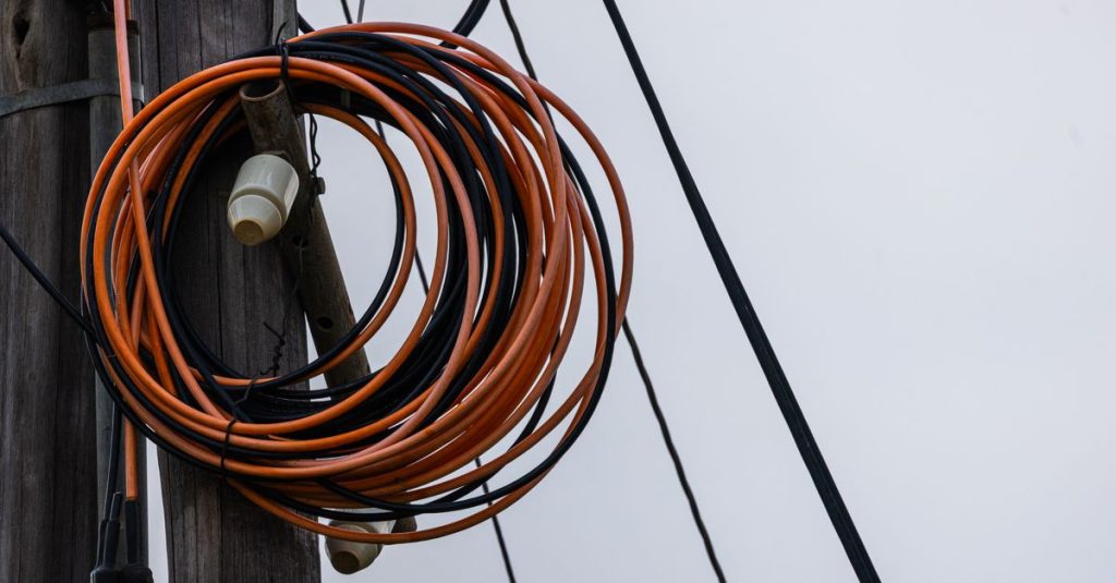 Close-up photo of coiled orange and black electrical wires on a wooden utility pole against a gray sky.