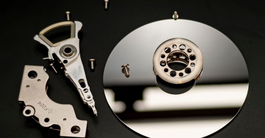 Close-up of dismantled hard drive parts with a reflection on a black surface, showcasing intricate mechanical details.