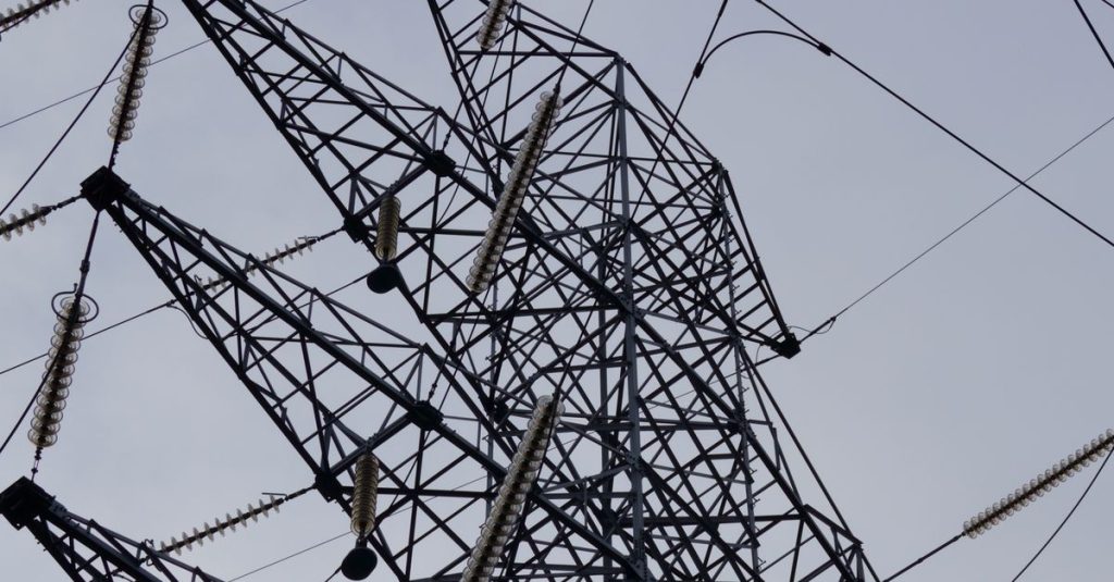 Low angle shot of a metal power transmission tower with cables against a clear sky.