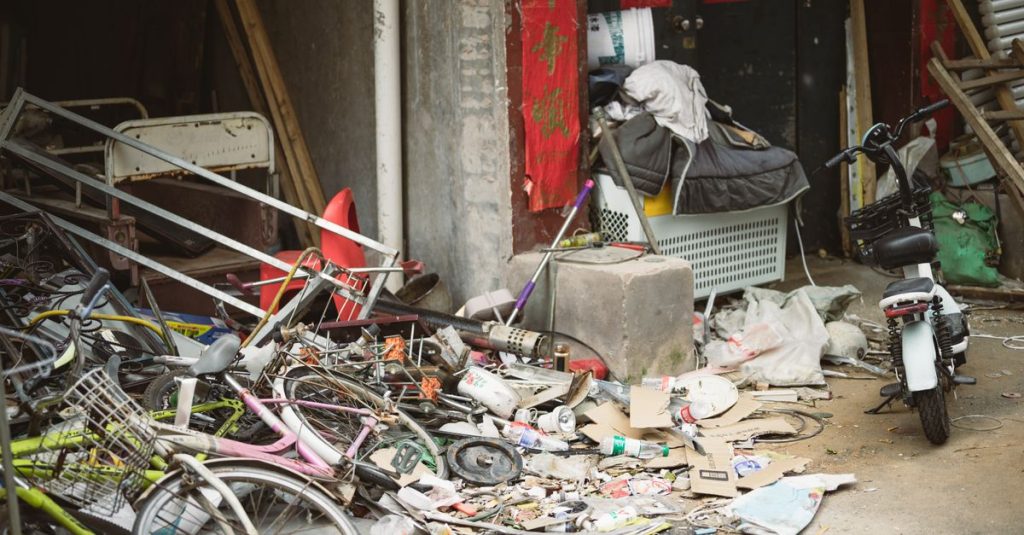 A cluttered alley filled with old bicycles, scrap metal, and miscellaneous debris beside a building.