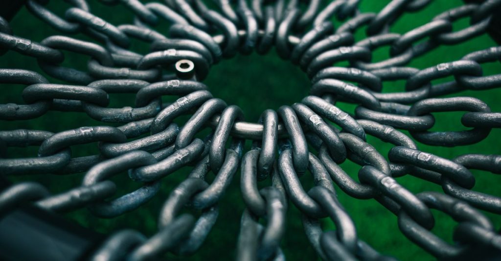 Top view of interwoven metal chains forming a circle against a green backdrop, creating a striking industrial pattern.