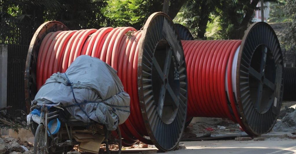 Image of large red industrial cable reels next to a covered tricycle on a sunny day.