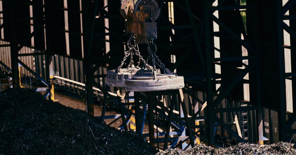 Overhead view of industrial magnet lifting scrap metal in recycling plant.