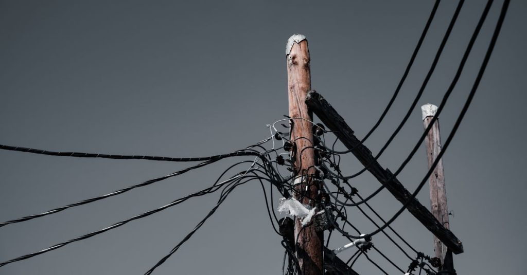 Low angle shot of wooden utility poles with power lines against a gray sky in Orlando, FL.
