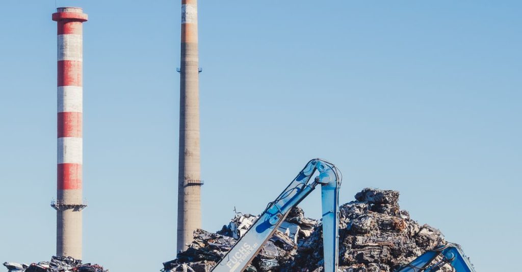 Industrial scrapyard with smokestacks and cranes on a clear day.