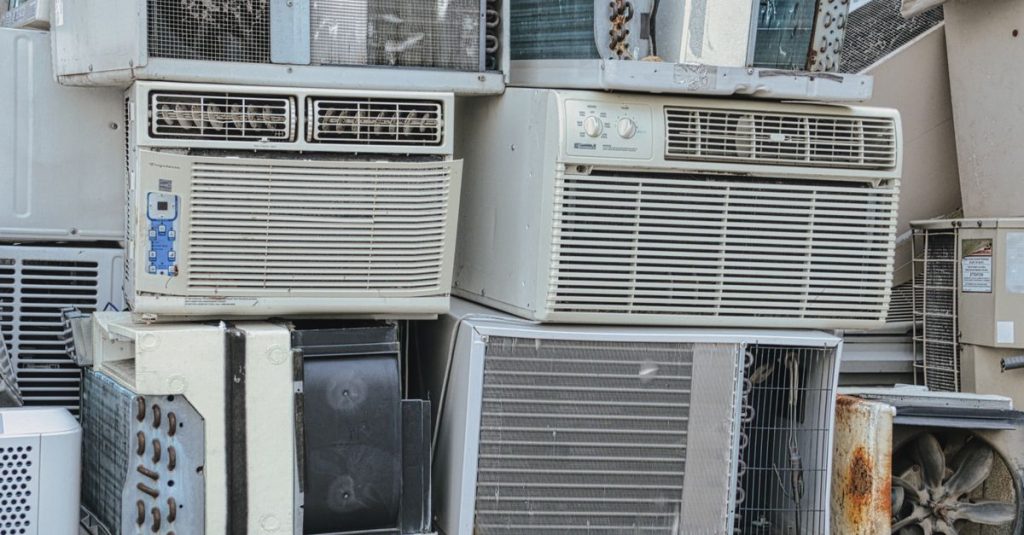 A pile of old window air conditioners awaits recycling, illustrating electronic waste issues.