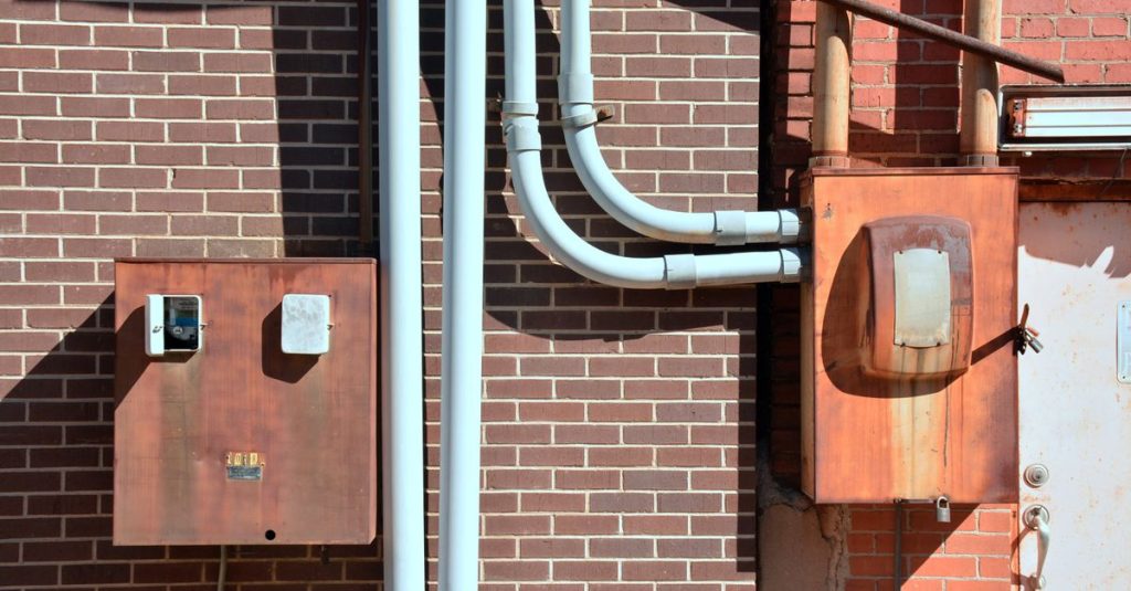 Close-up of industrial utility boxes and piping on a brick wall in Texarkana, Texas.