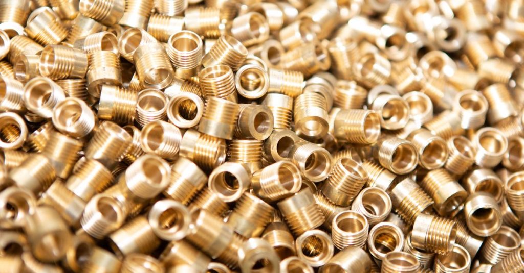 Uzundere Hurdacı A detailed close-up of a pile of brass screws and nuts with a golden metallic finish.