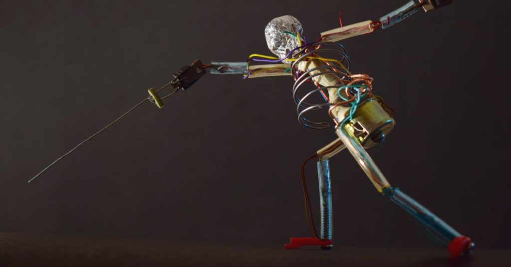 Metallic robot sculpture in a dynamic fencing pose with wires and parts, shot in São Paulo.