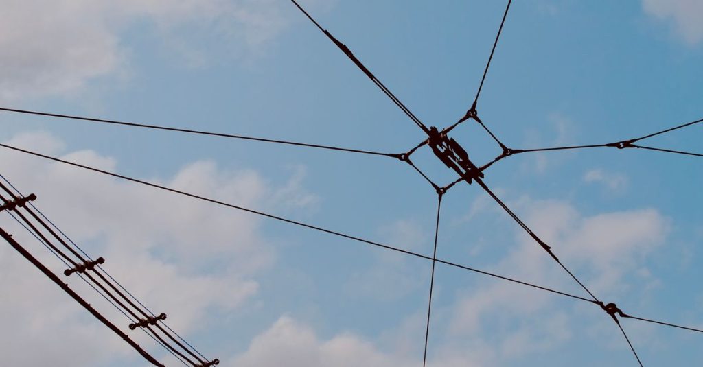 A network of power lines stretching across a blue sky with clouds.