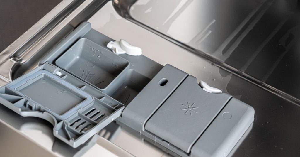 A detailed view of a dishwasher detergent compartment with soap residue.