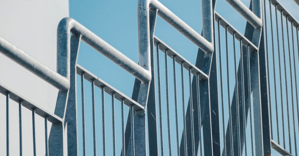 Close-up of a modern staircase railing against a bright blue sky, showcasing urban architecture.