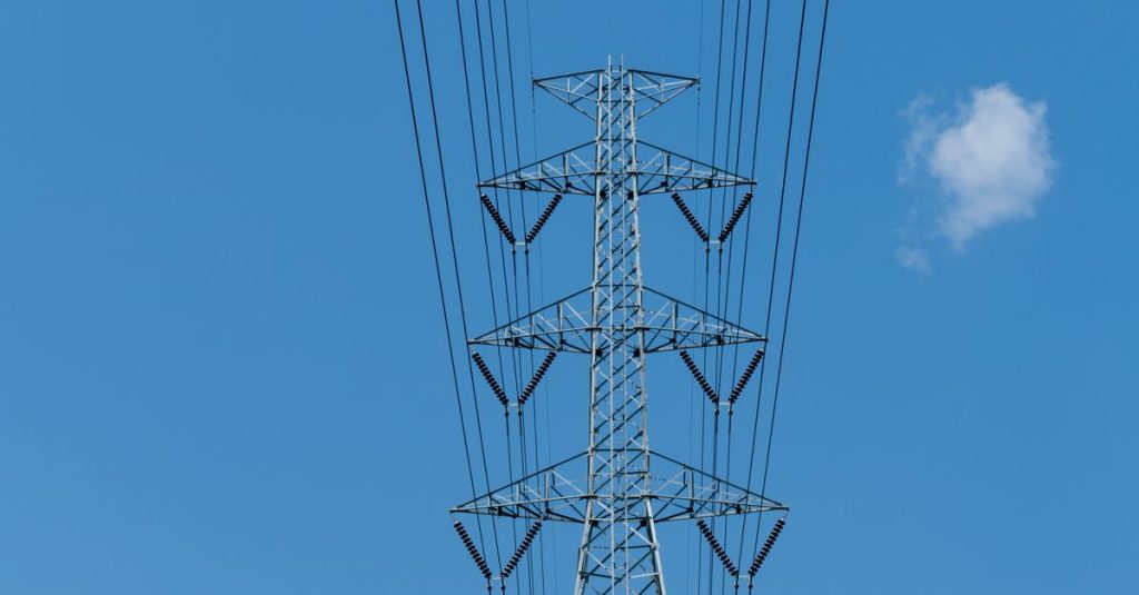 Low angle view of electric transmission tower and power lines under blue sky.
