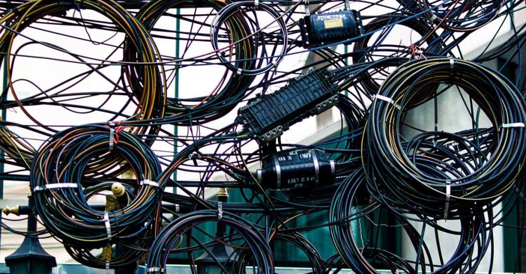 Intricate network of tangled power and communication cables outdoors.