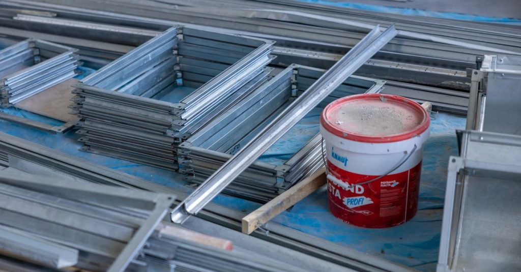 Stacks of metal frames and a paint bucket inside a construction site emphasizing building materials.