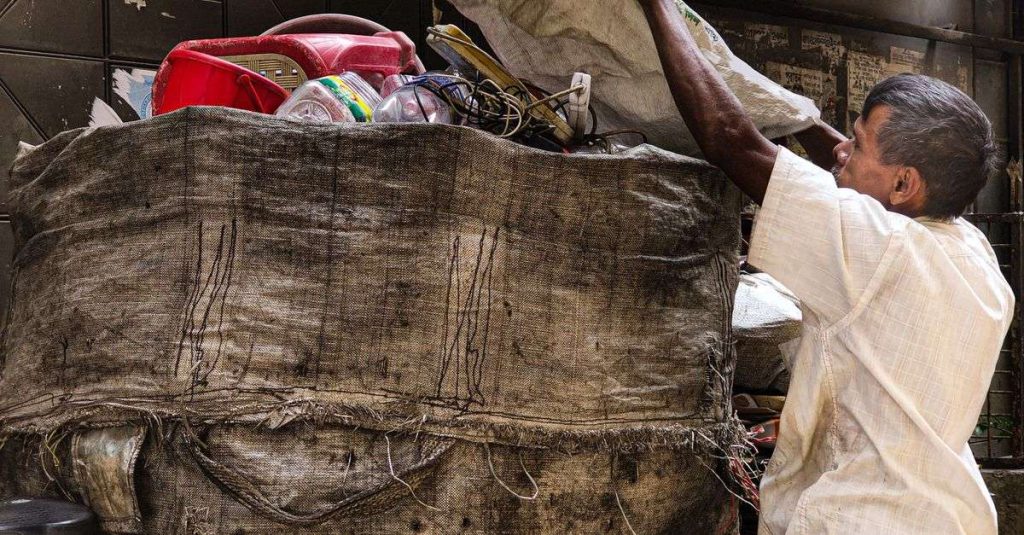 An adult casually sorts recyclable materials in a large sack on an urban street.